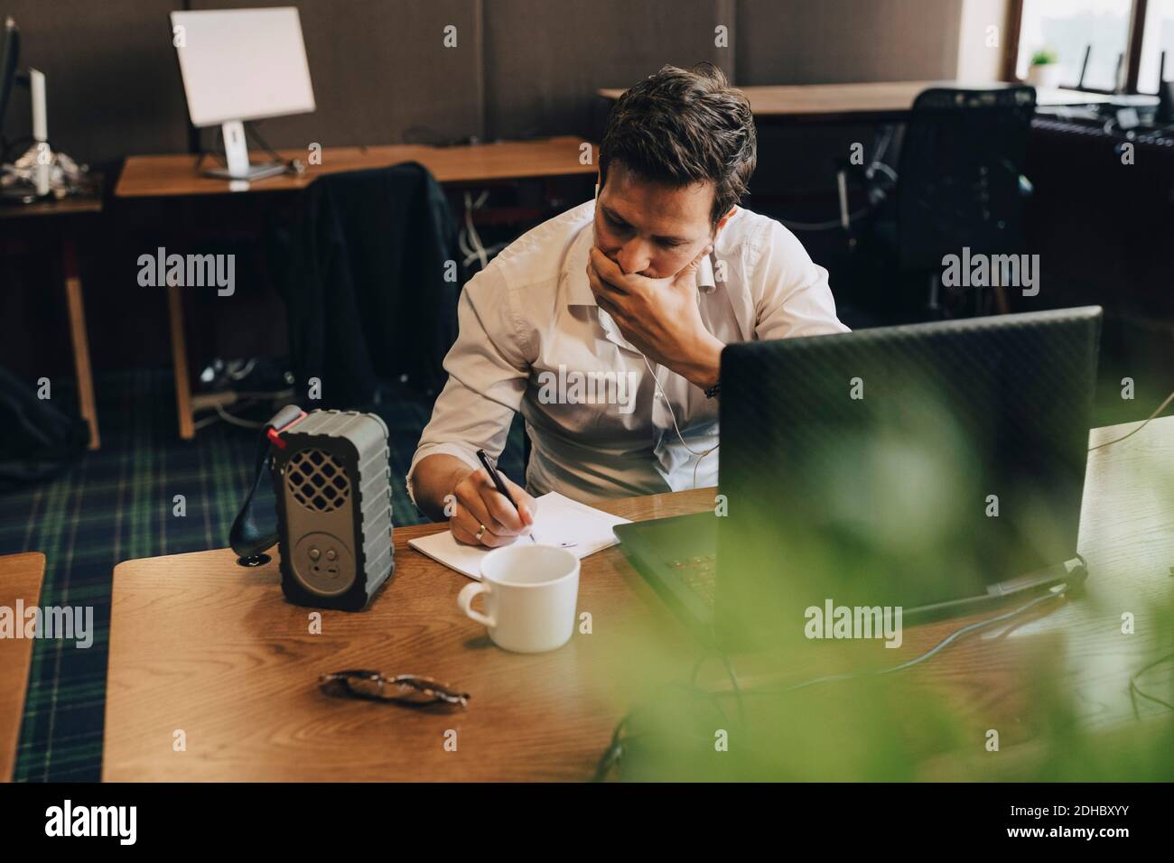 Ein Geschäftsmann, der am Schreibtisch in Papier schreibt, deckt den Mund Stockfoto