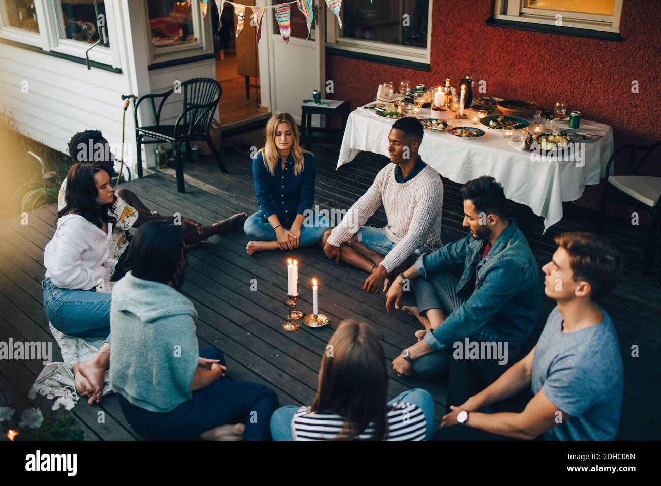 High-Angle-Ansicht von männlichen und weiblichen Freunden sitzen mit Augen geschlossen um brennende Kerzen auf dem Balkon während der Gruppentherapie S Stockfoto