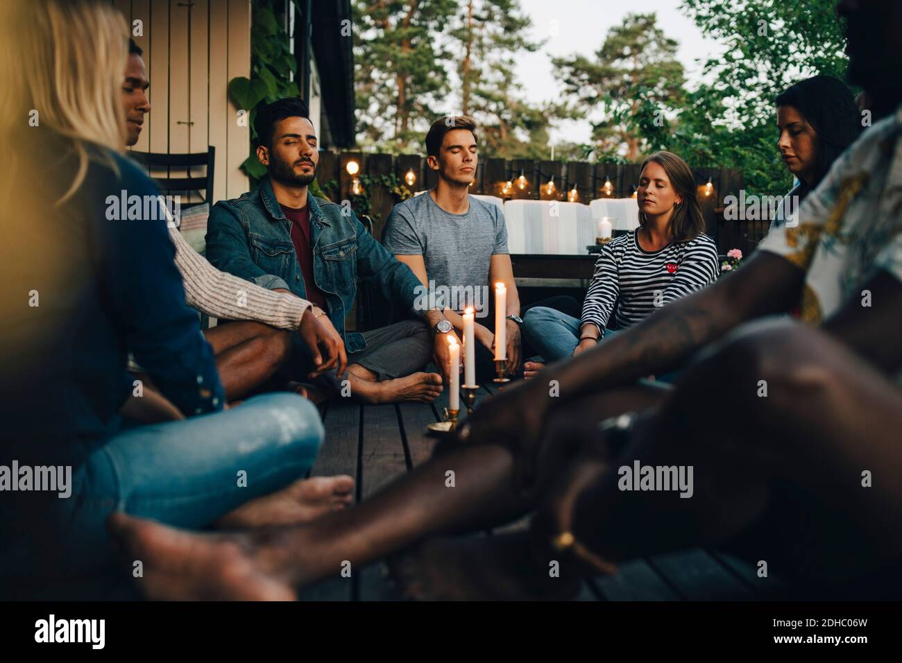 Männliche und weibliche Freunde sitzen mit geschlossenen Augen auf dem Balkon Während der Gruppensitzung Stockfoto