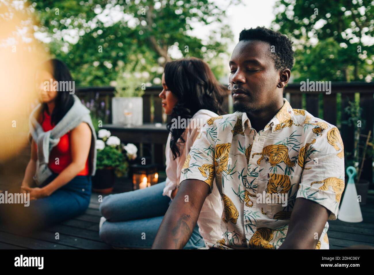 Multiethnische Freunde, die während der Gruppe mit geschlossenen Augen auf dem Balkon sitzen Sitzung am Wochenende Stockfoto