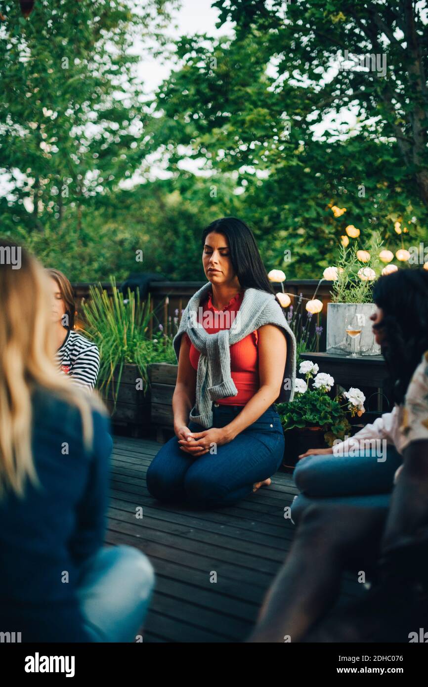 Mittlere Erwachsene Frau, die mit geschlossenen Augen von Freunden sitzt Balkon während der Gruppensitzung Stockfoto