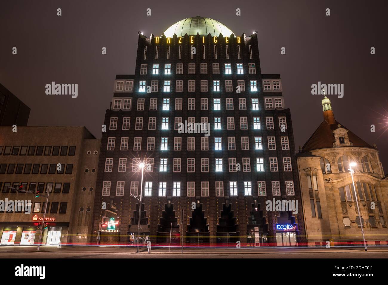 Hannover, Deutschland. Dezember 2020. Beleuchtete Fenster lassen im Rahmen eines Adventkalenders die Zahl 10 an der Fassade des Anzeiger-Hochhauses erstrahlen - Autos fahren abends am Denkmal vorbei (Aufnahme mit langer Belichtungszeit). Quelle: Moritz Frankenberg/dpa/Alamy Live News Stockfoto