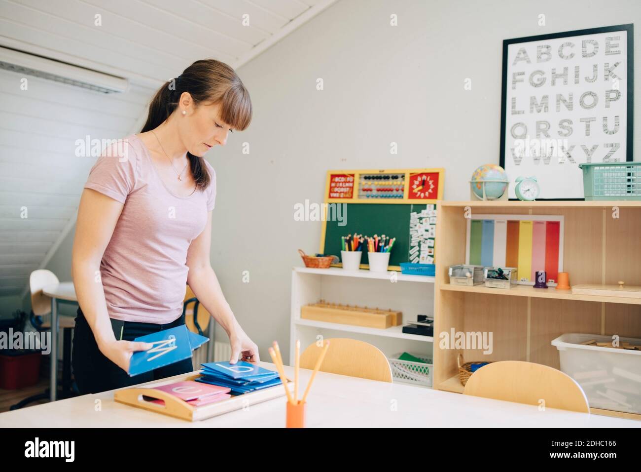 Selbstbewusste mittlere Erwachsene Lehrerin Anordnung Flash-Karten mit Alphabeten Am Tisch im Klassenzimmer Stockfoto