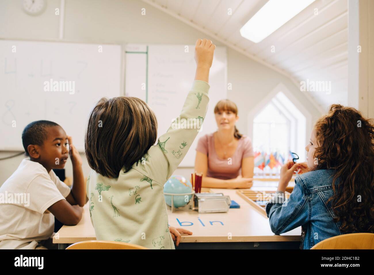 Schuljunge Hand heben, während Antwort Lehrer im Klassenzimmer in der Schule Stockfoto