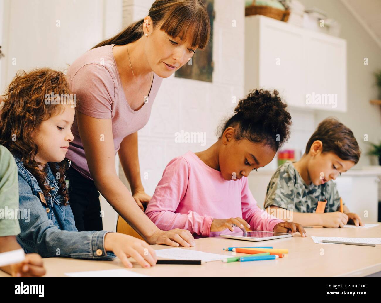 Lehrer führt männliche und weibliche Schüler am Schreibtisch im Klassenzimmer Stockfoto