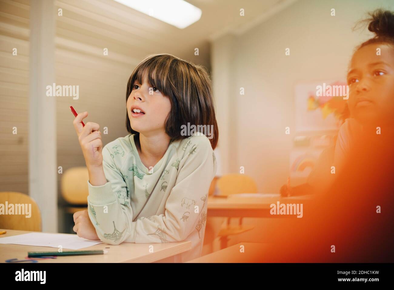 Neugieriger Junge, der am Schreibtisch sitzt, während er sich im Klassenzimmer konzentriert Stockfoto