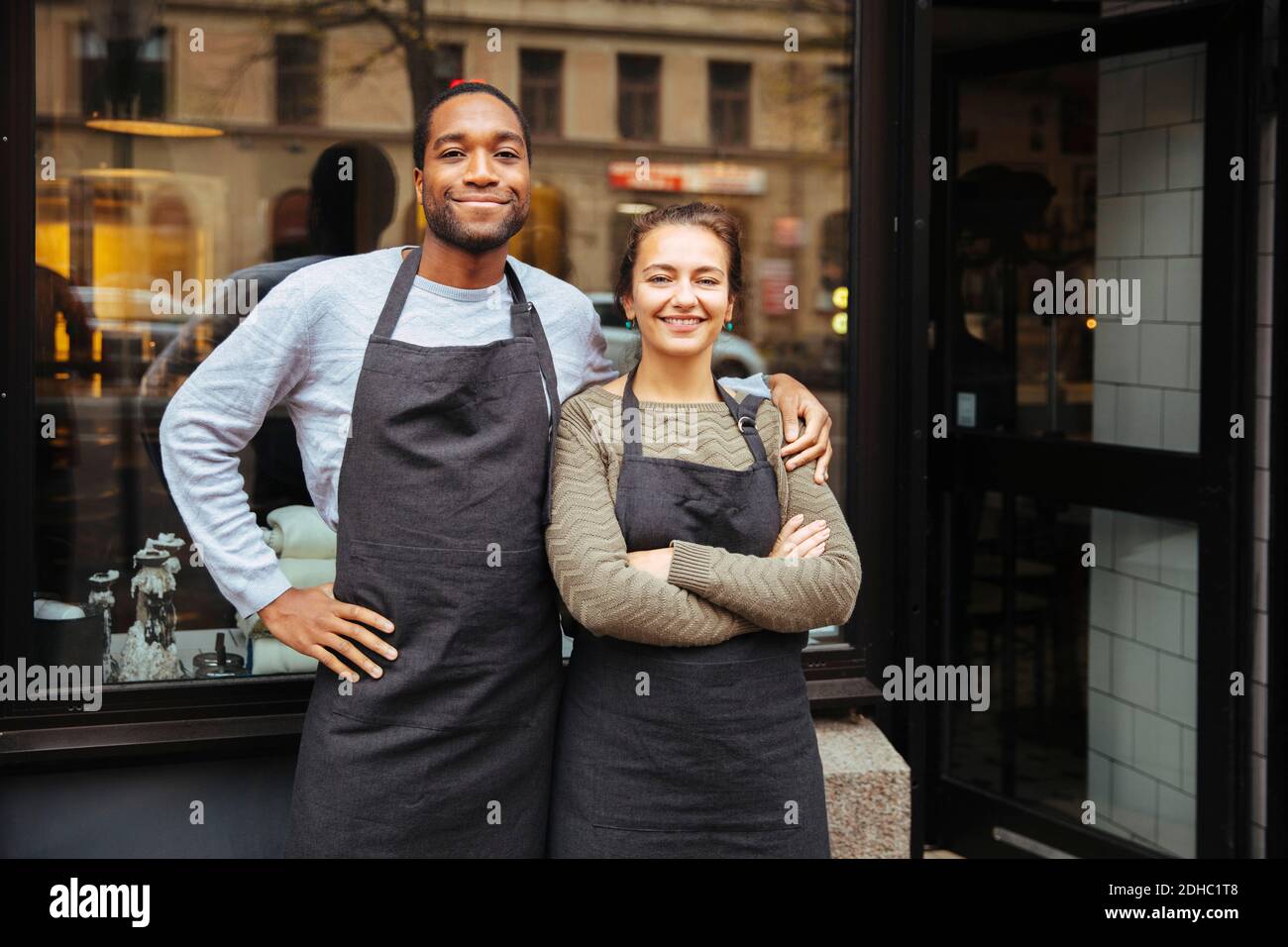 Porträt von selbstbewussten jungen Besitzern, die gegen Feinkostfenster stehen Stadt Stockfoto