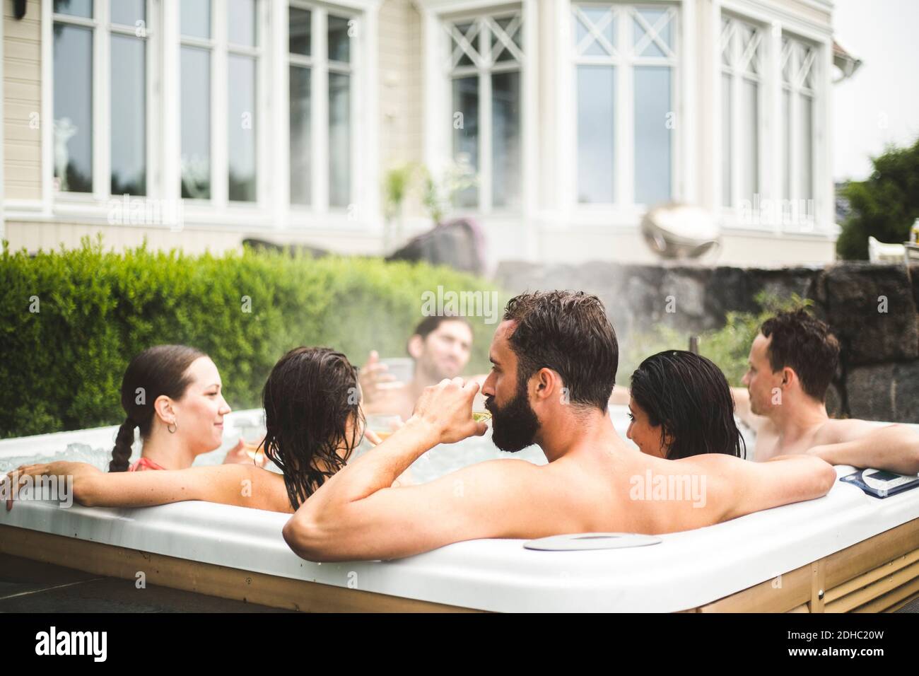Mittlerer Erwachsener Mann, der Alkohol trinkt, während er mit Freunden in genießt Wannen-Whirlpool am Wochenende Stockfoto