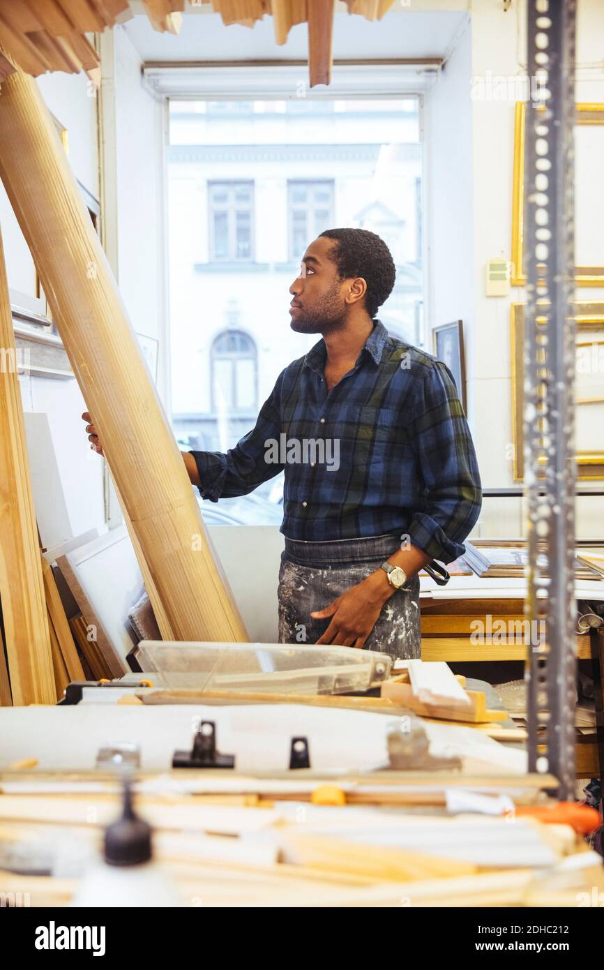 Selbstbewusster junger Handwerker, der Holz in der Rahmwerkstatt betrachtet Stockfoto