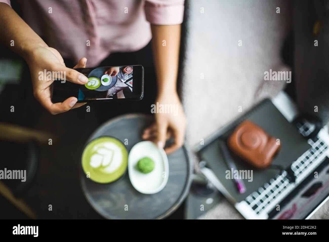 Mittelteil der Bloggerin fotografieren Matcha Tee und Snack durch Smartphone im kreativen Büro Stockfoto