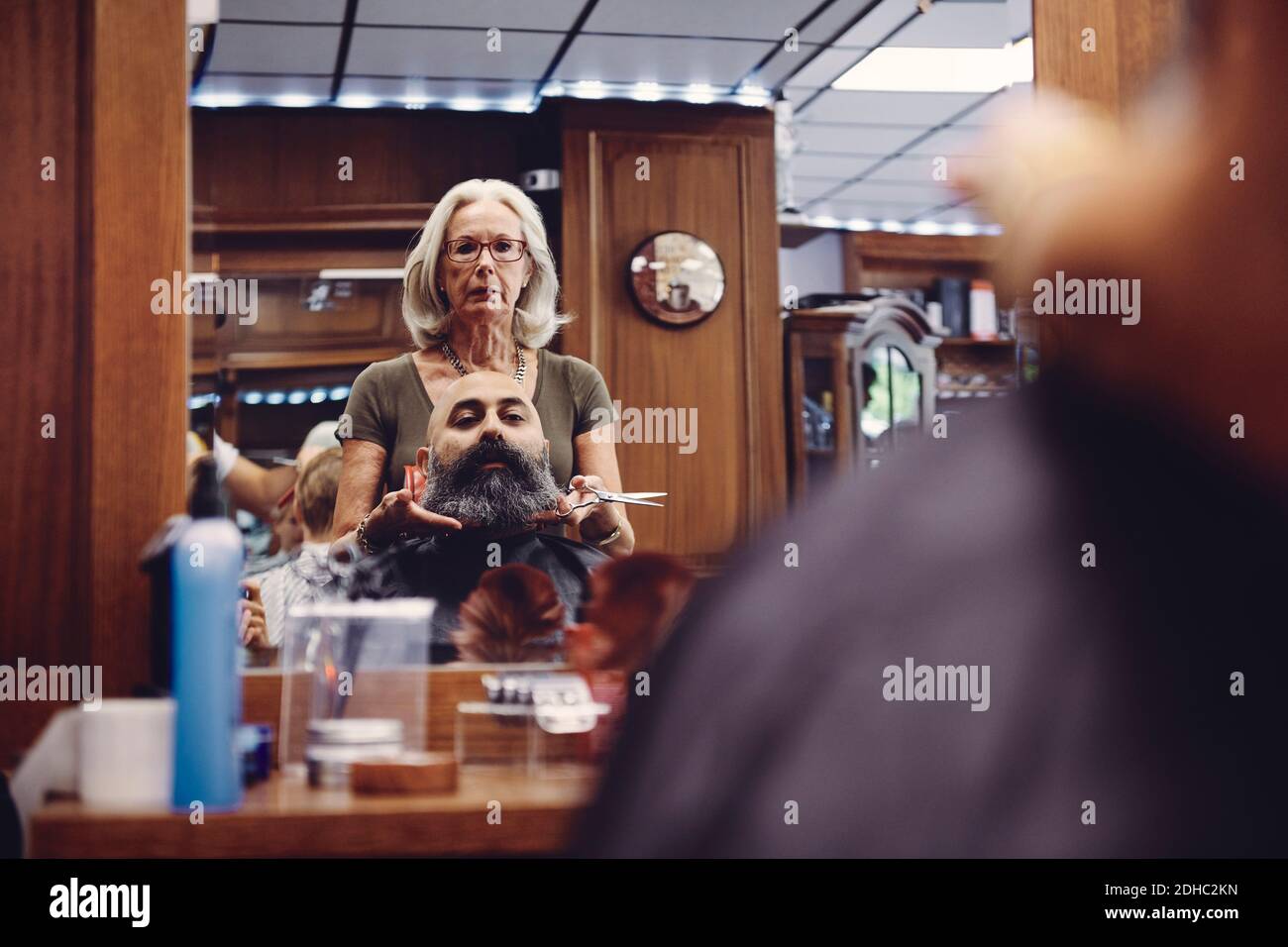 Spiegelung der weiblichen Friseur Trimmen Bart des mittleren erwachsenen Mann Im Salon Stockfoto