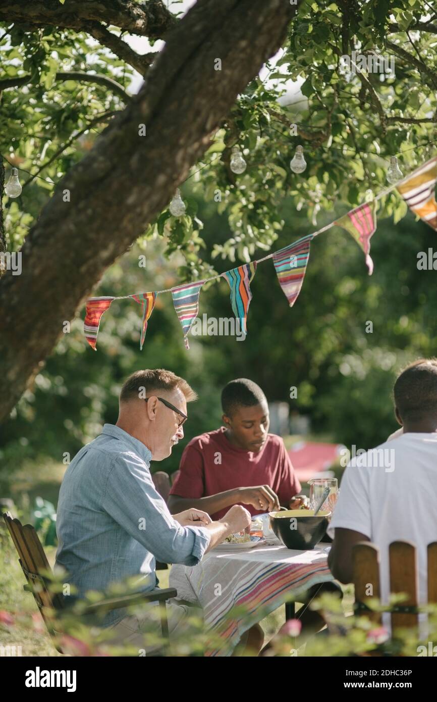 Junge essen Mittagessen mit Vater und Großvater auf der Terrasse während Gartenparty Stockfoto