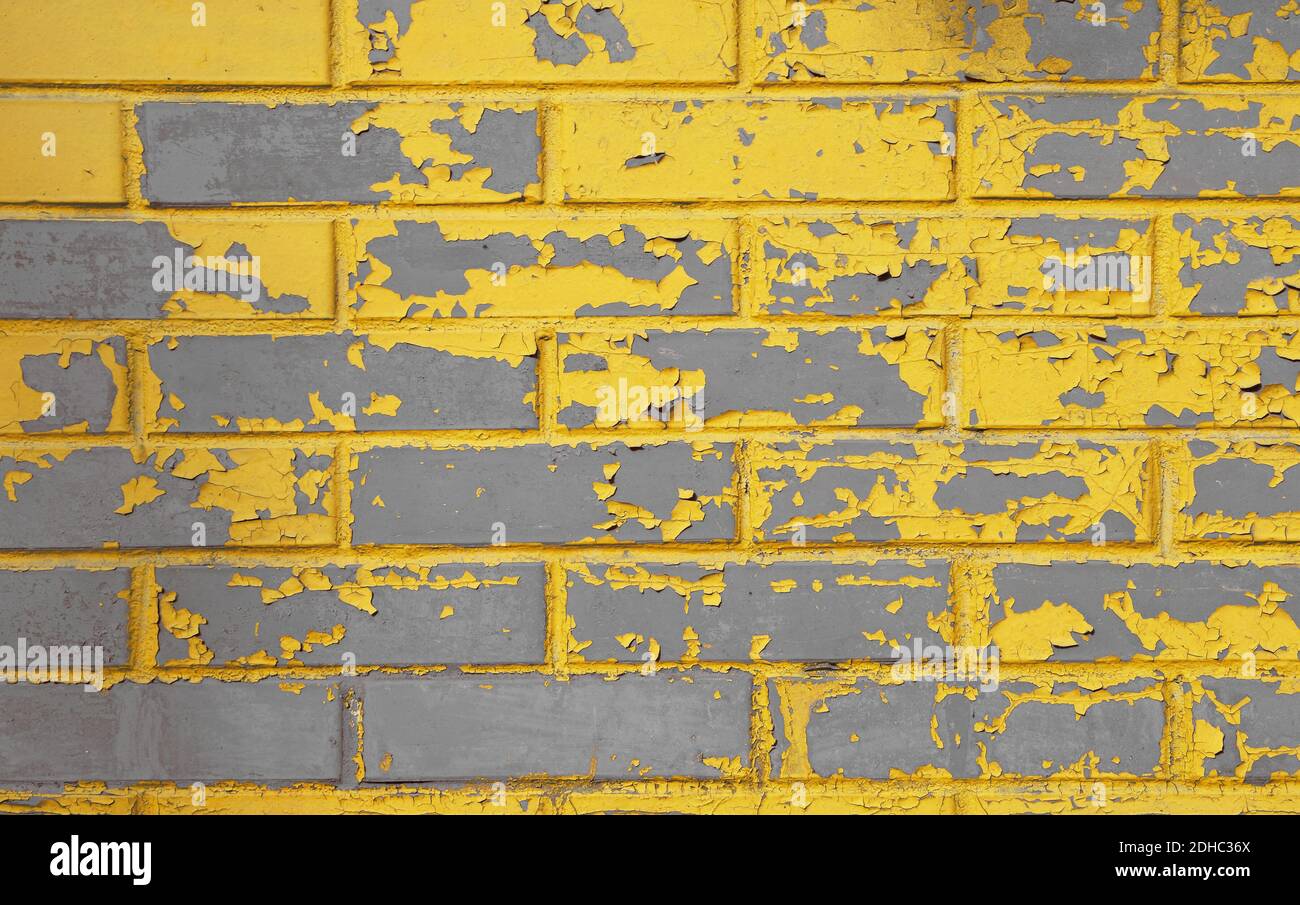 Alte Grunge verwitterte graue Betonmauer mit schuppigen gelben Farbflecken, Flecken und Defekten Stockfoto