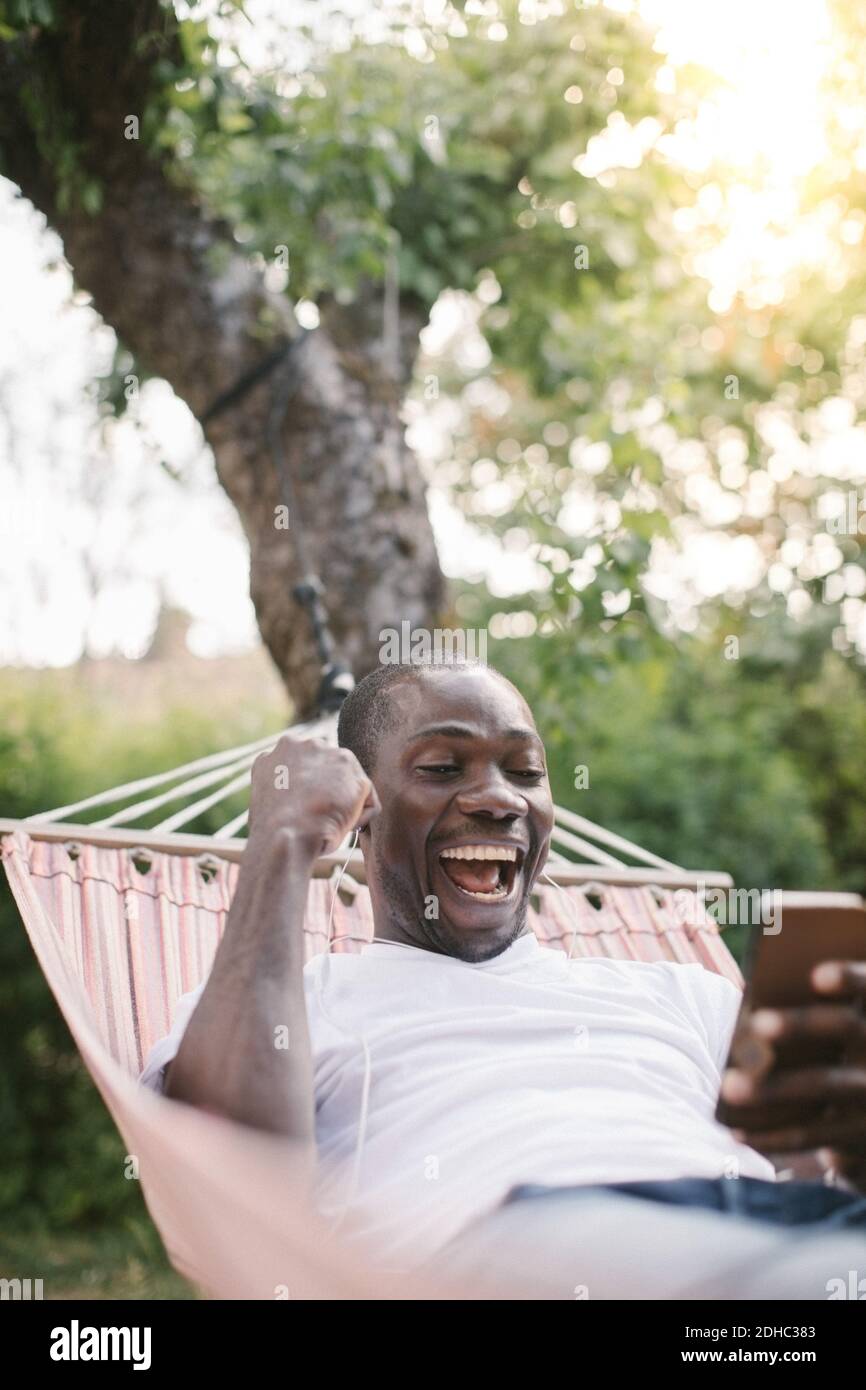Ein fröhlicher Mann mittleren Erwachsenen, der beim Entspannen auf das Handy schaut Auf Hängematte im Hinterhof Stockfoto