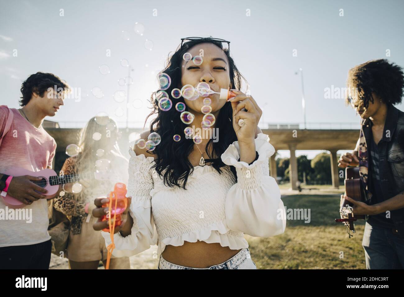 Frau bläst Seifenblasen, während Freunde spielen Ukulele während der Musik Ereignis Stockfoto