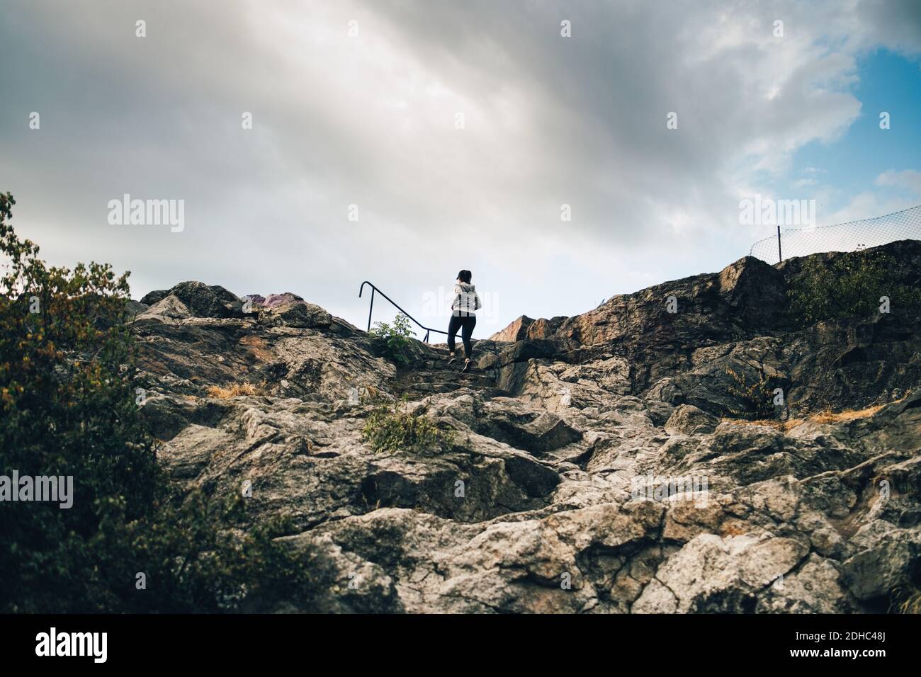Low-Angle-Ansicht der weiblichen Sportlerin Klettern Felsen auf Hügel Gegen den Himmel Stockfoto