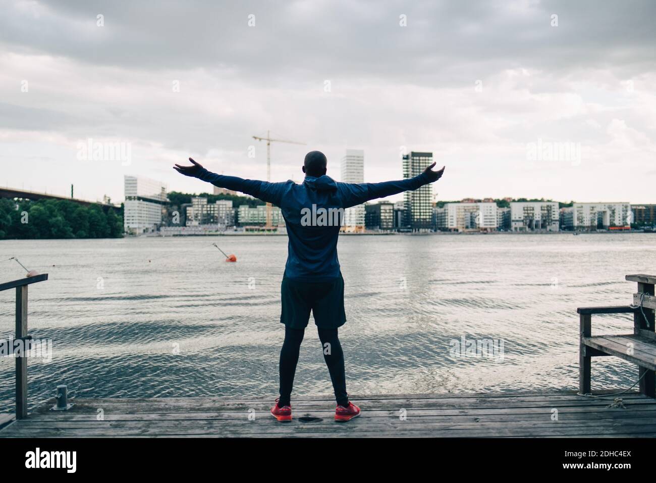 Rückansicht des männlichen Athleten, der mit ausgestreckten Armen steht pier über Meer in der Stadt Stockfoto