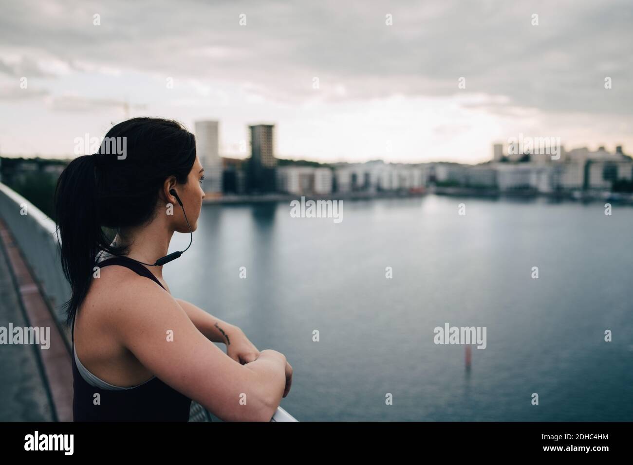 Seitenansicht einer Sportlerin, die im Stehen die Stadt anschaut Auf einer Fußgängerbrücke über das Meer Stockfoto