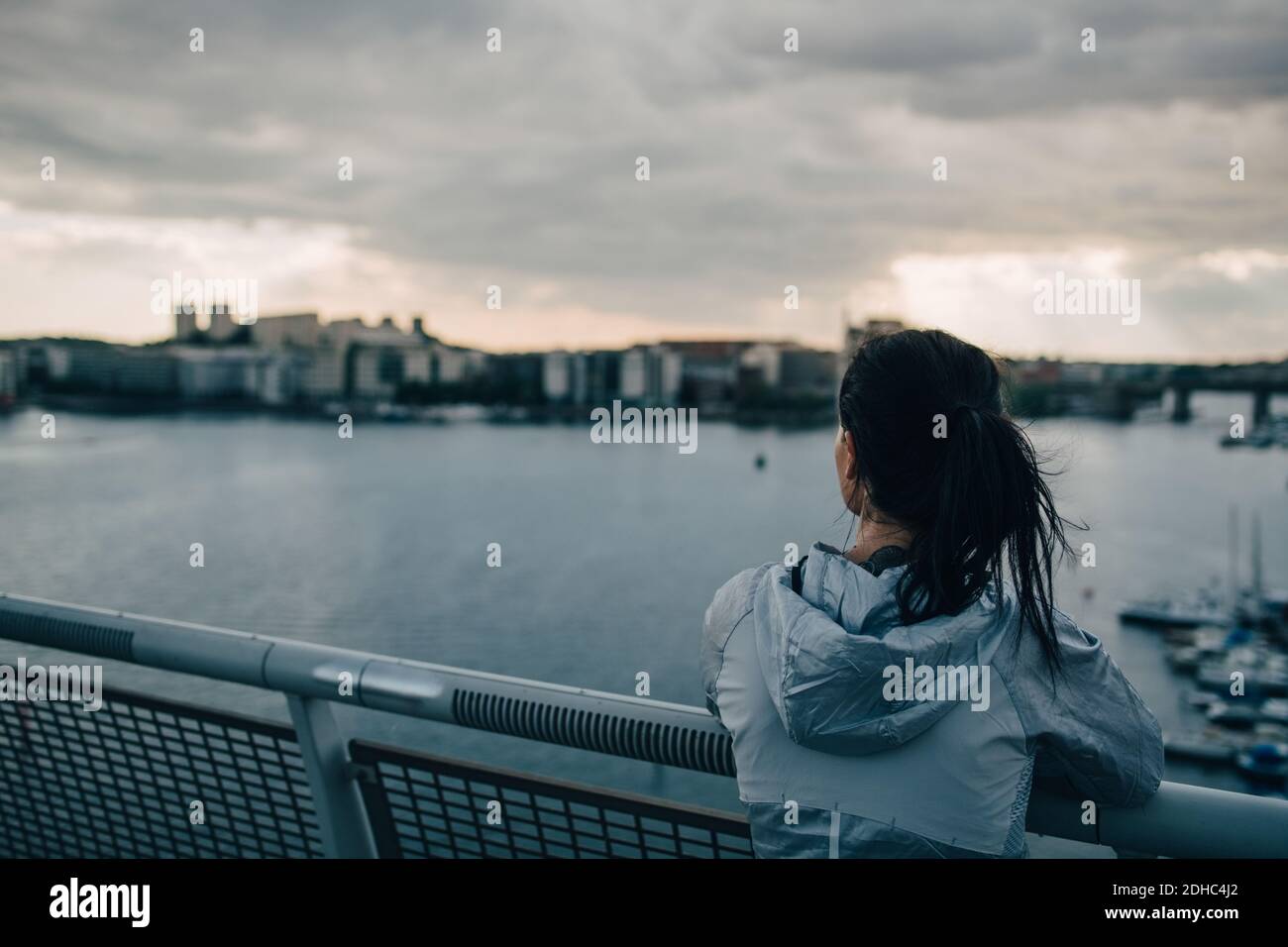 Rückansicht einer Sportlerin, die auf der Stadt steht Fußgängerbrücke über das Meer bei Sonnenuntergang Stockfoto
