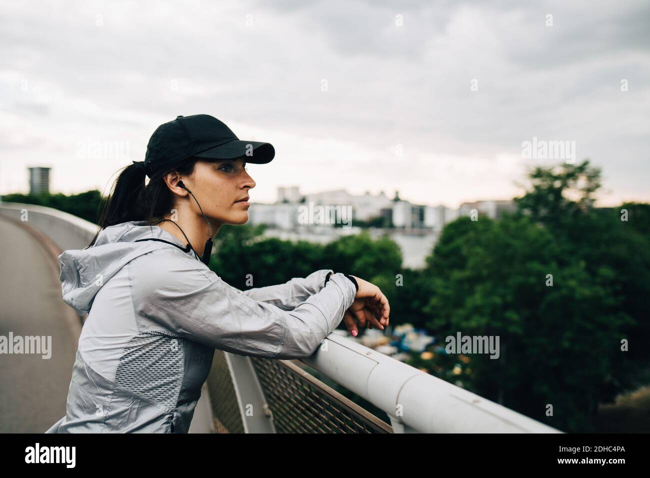 Müde Sportlerin schaut weg, während sie sich auf dem Geländer am Steg lehnt In der Stadt Stockfoto