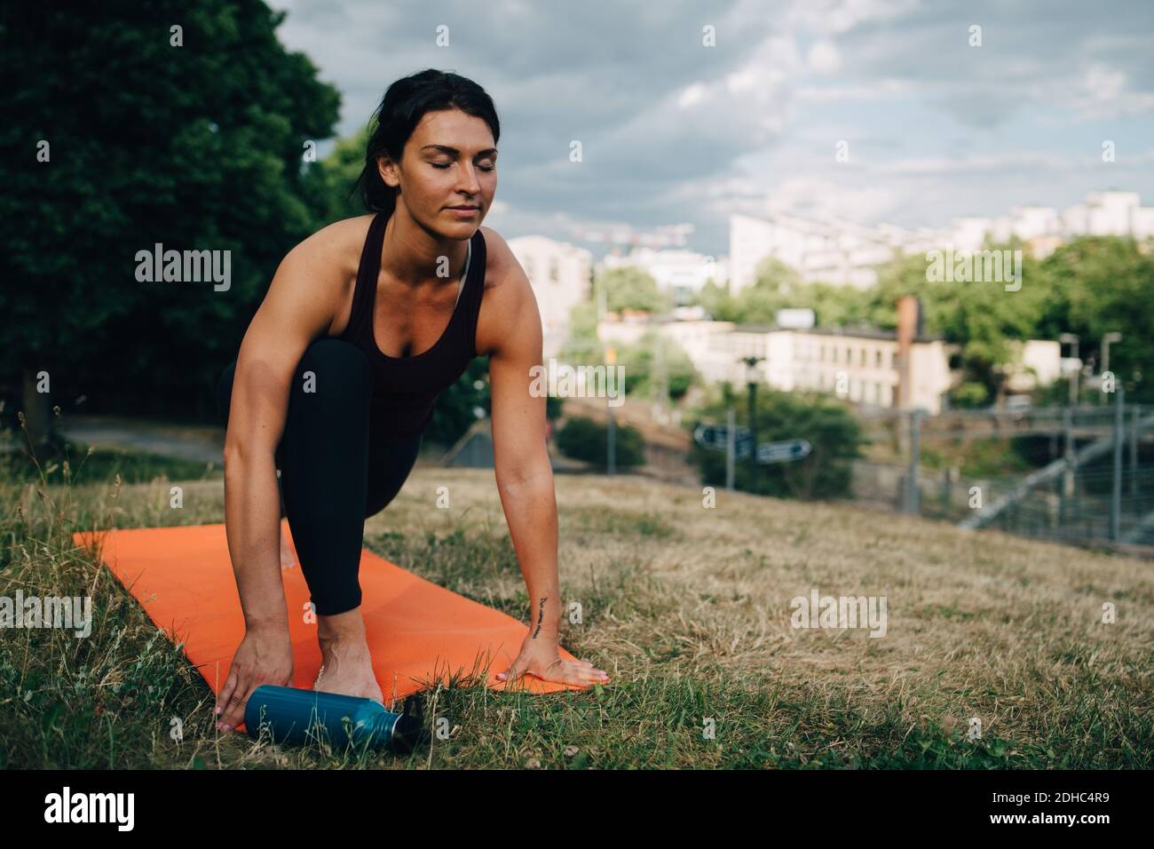 Junge Frau mit geschlossenen Augen praktiziert Yoga auf Feld in Stadt Stockfoto