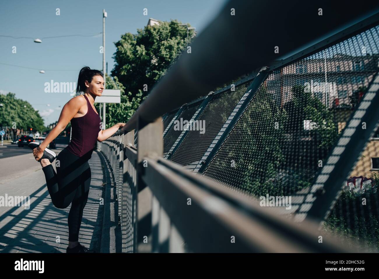 Junge Sportlerin streckt Bein durch Geländer auf Brücke in der Stadt Stockfoto