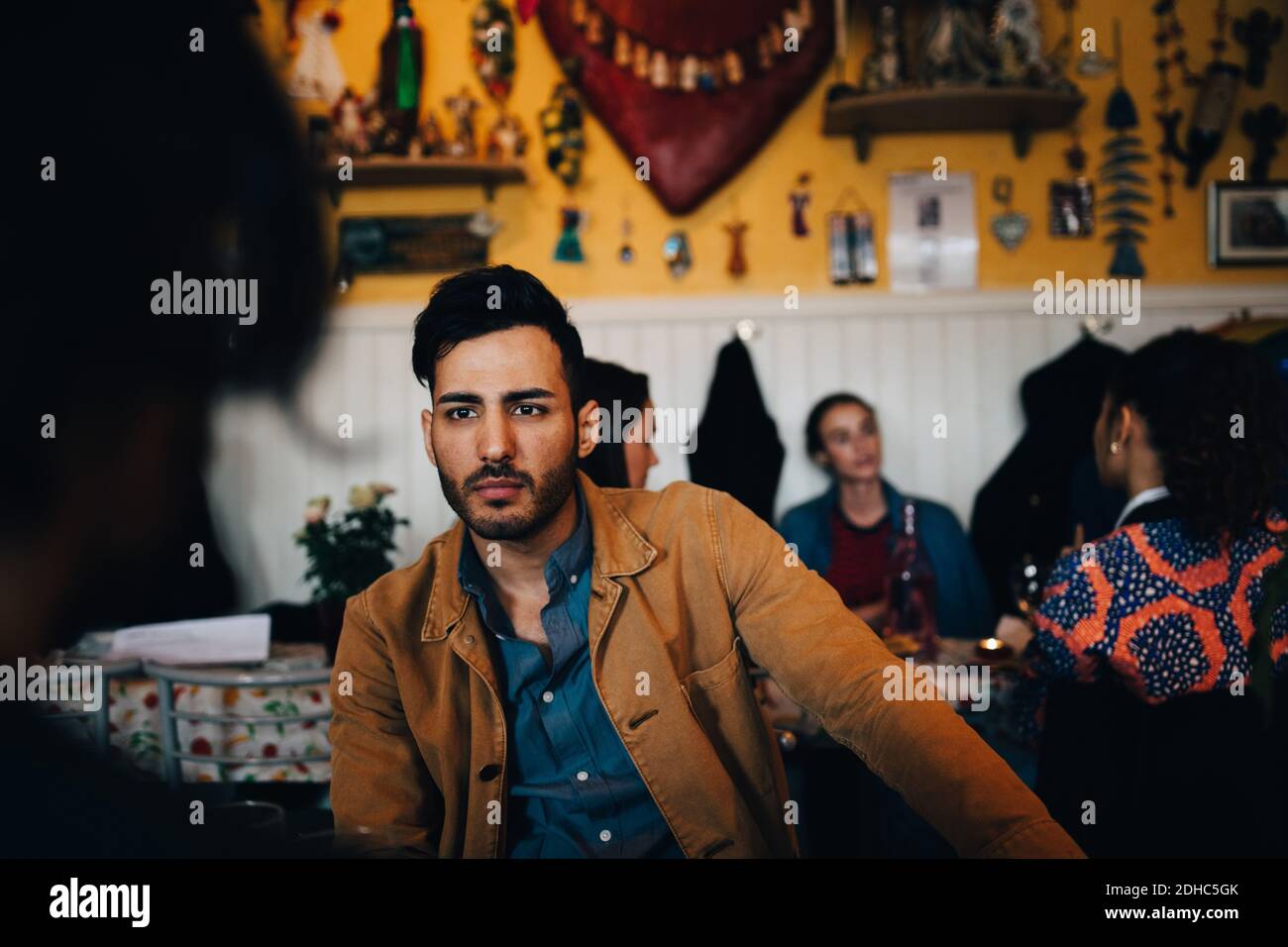 Junger Mann, der Freund ansieht, während er gegen Frauen sitzt Restaurant während des Brunchs Stockfoto