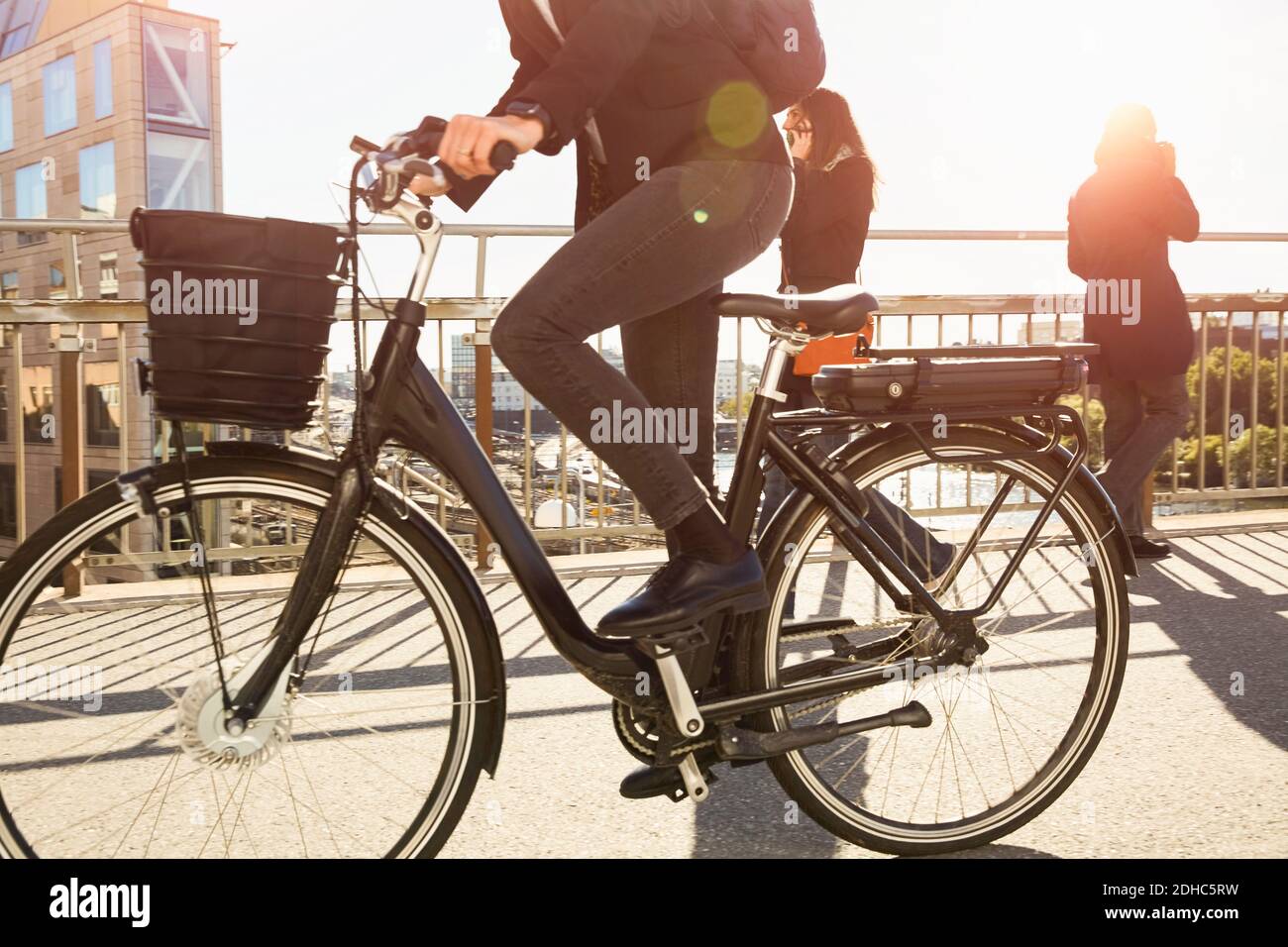 Niedriger Abschnitt der reifen Frau Reiten Elektro-Fahrrad von Pendlern Auf der Brücke in der Stadt gegen den Himmel Stockfoto