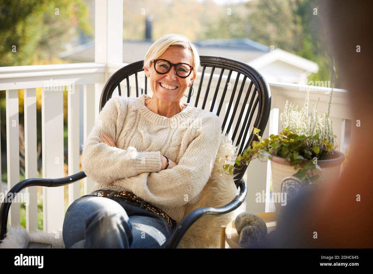 Portrait der fröhlichen reifen Frau mit gekreuzten Armen sitzend auf Veranda Stockfoto