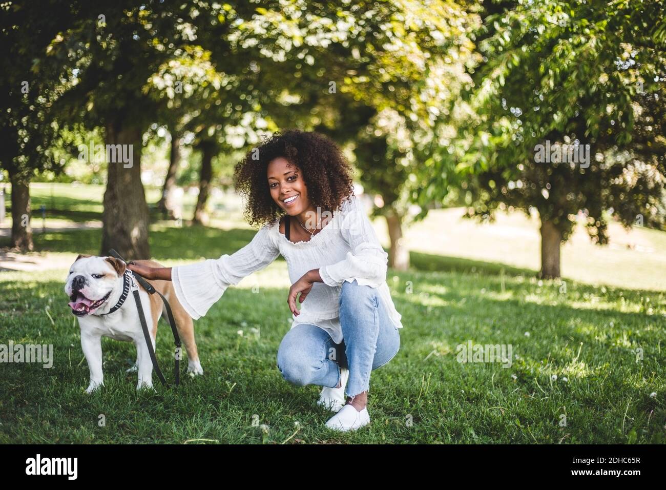 Porträt einer lächelnden Frau mit Bulldogge auf grasbewachsenem Feld bei parken Stockfoto