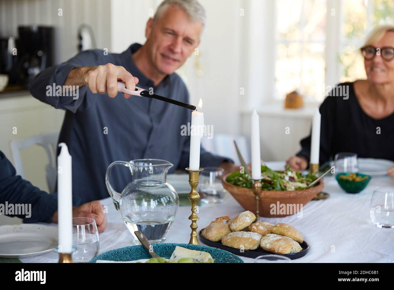 Reifer Mann zündet Kerze auf Esstisch von Freund an Zu Hause Stockfoto