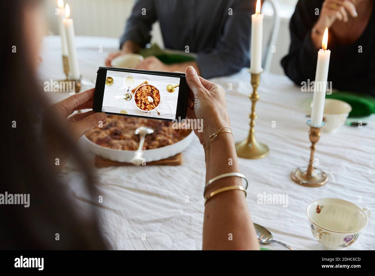 Reife Frau mit Smartphone beim Mittagessen mit Freunden Zu Hause Stockfoto