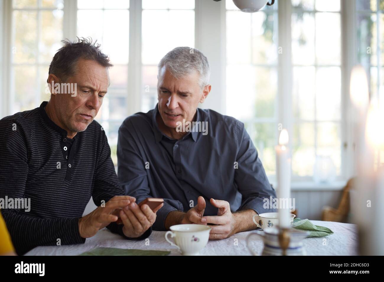Ernst reifen Mann zeigt Handy an Freund während sitzen Am Esstisch Stockfoto