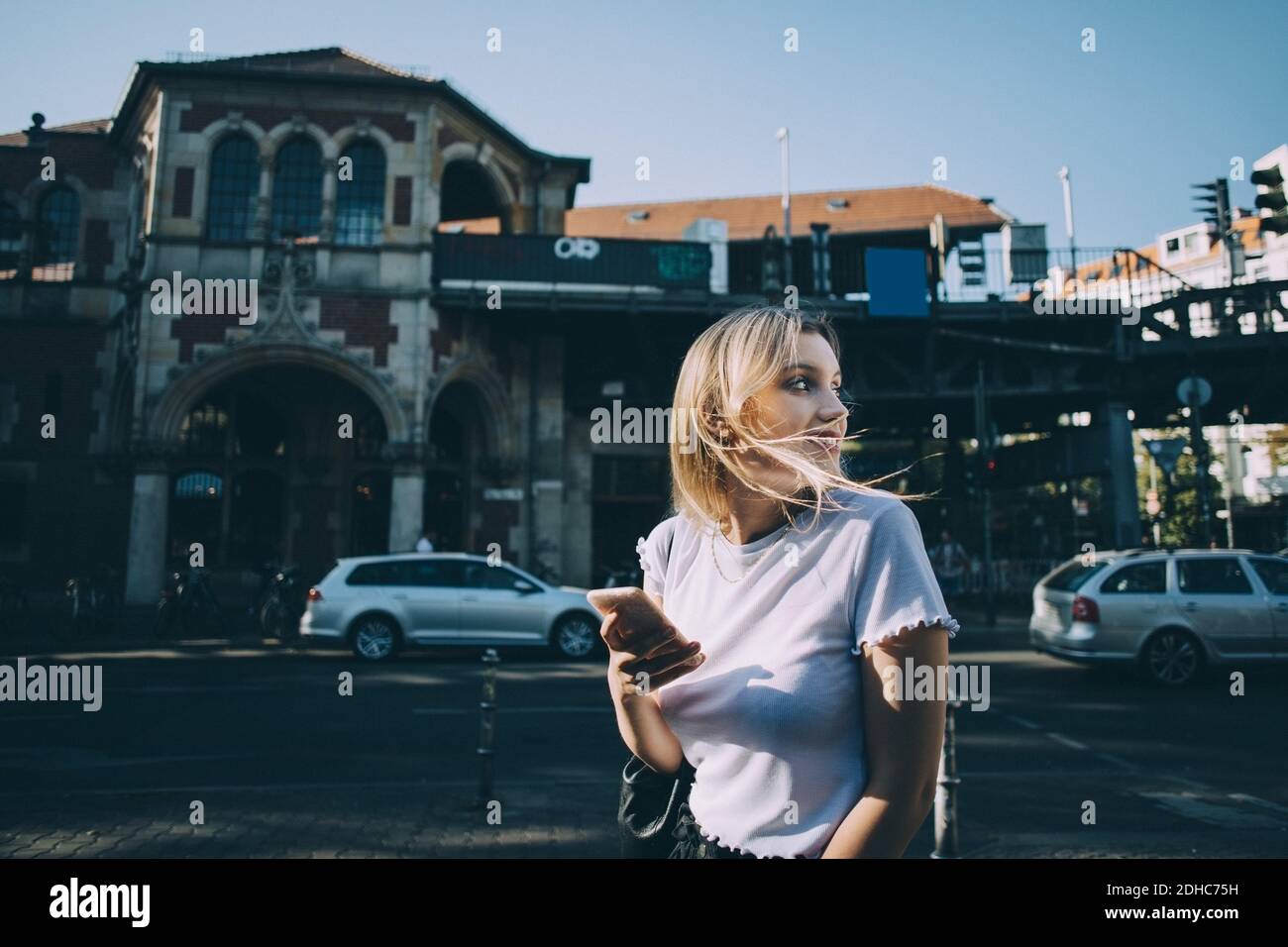 Junge Frau, die über die Schulter schaut und dabei das Mobiltelefon anhält Straße in der Stadt Stockfoto