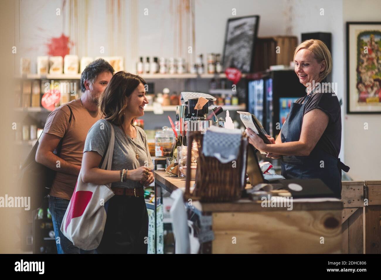 Lächelnde Verkäuferin, die während der Kundschaft Lebensmittel betrachtet Am Schalter stehen Stockfoto