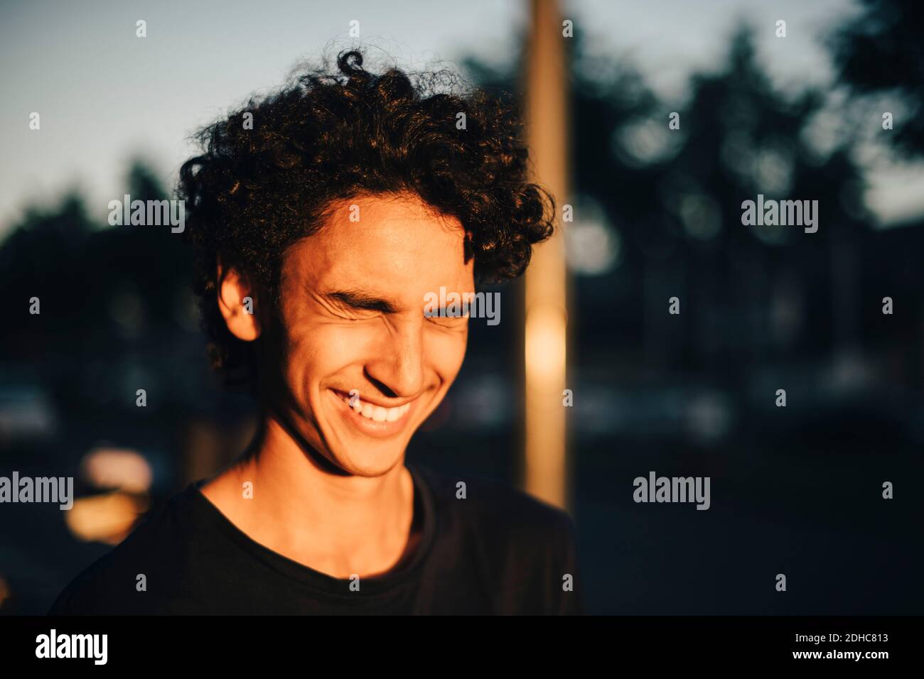 Fröhlicher Teenager-Junge mit geschlossenen Augen in der Stadt während des Sonnenuntergangs Stockfoto