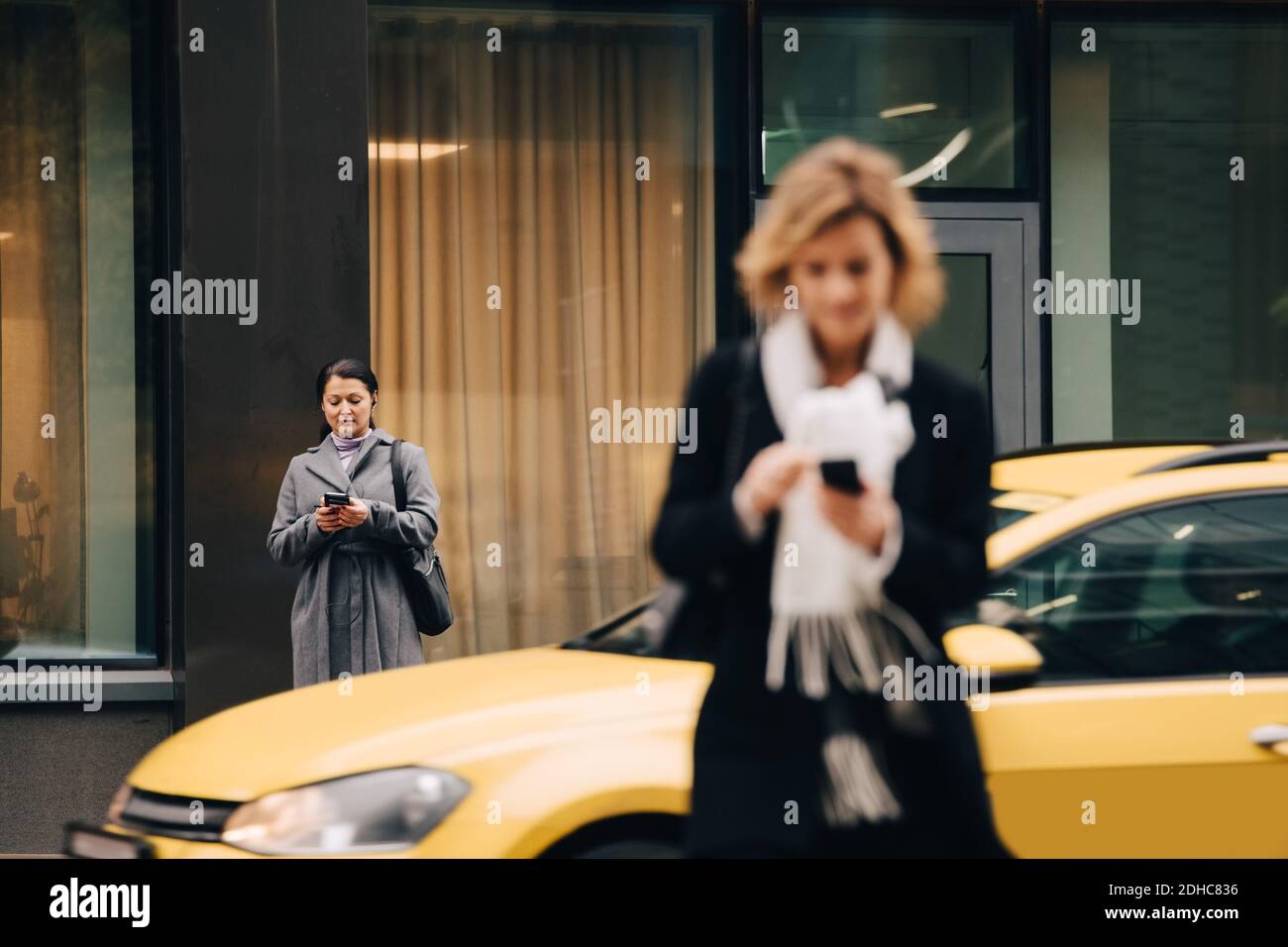 Geschäftsfrauen, die Smartphones benutzen, während sie auf der Straße gegen Gebäude stehen In der Stadt Stockfoto