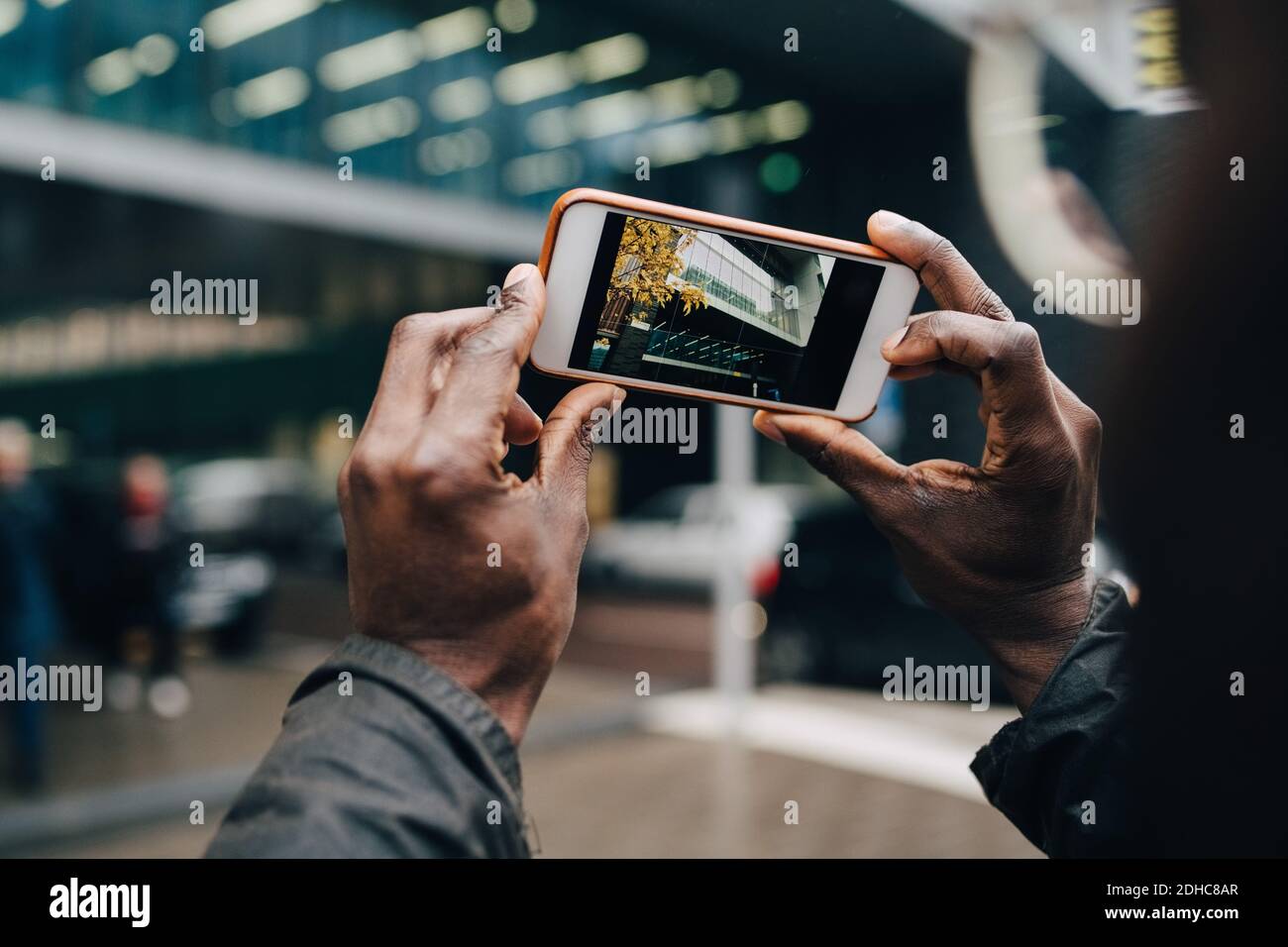 Verkürzte Hände eines Geschäftsmannes, der Gebäude mit einem Smartphone fotografiert Stadt Stockfoto