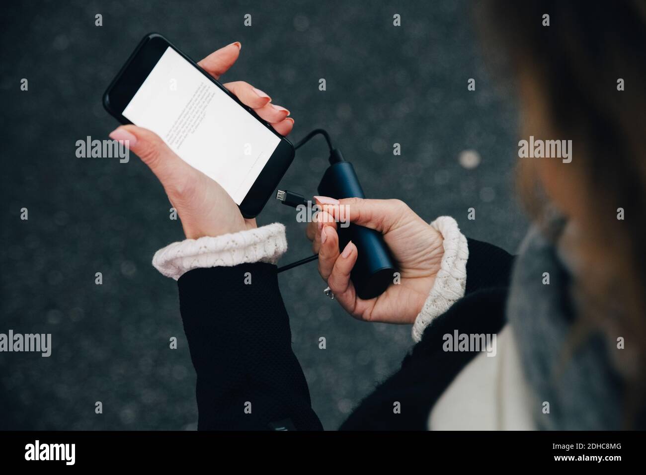 Mittelteil der Geschäftsfrau beim Einsetzen des Ladegeräts in das Mobiltelefon im Stehen Auf der Straße Stockfoto