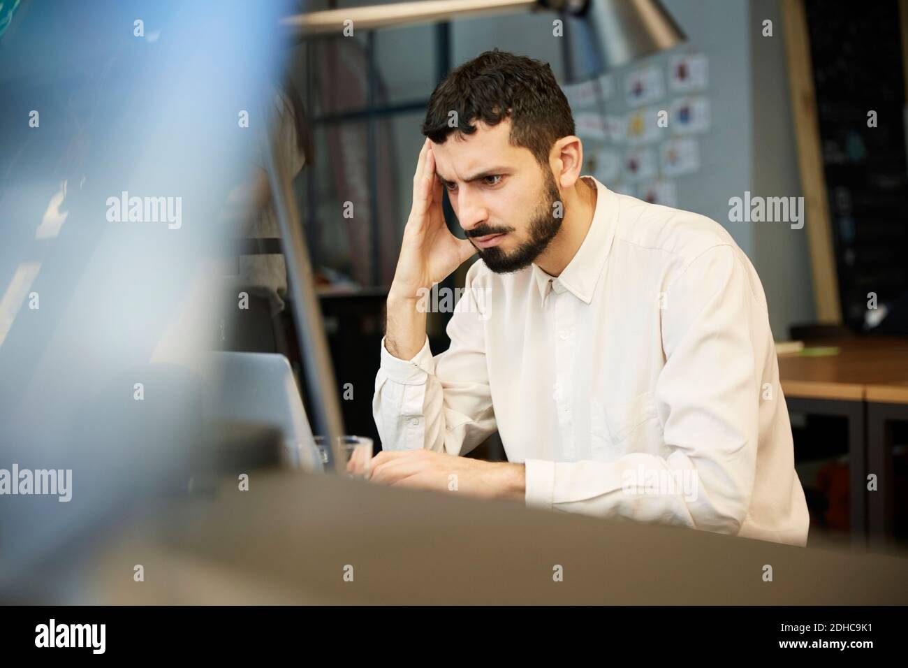 Angespannter Geschäftsmann mit Blick auf Laptop, während er im kreativen Büro sitzt Stockfoto