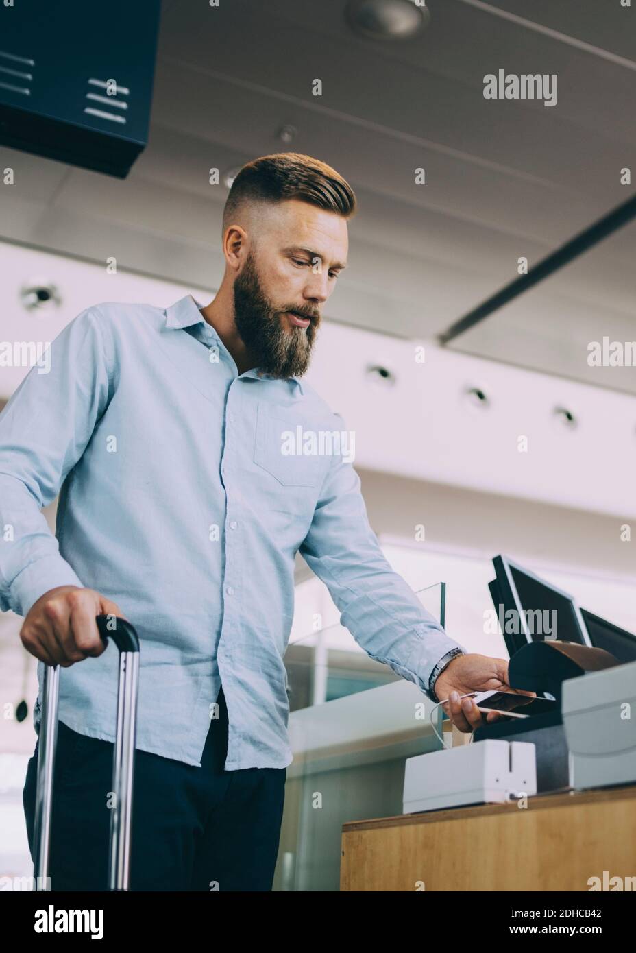 Low-Winkel-Ansicht des Geschäftsmannes Scannen Ticket auf dem Smartphone Am Check-in-Schalter am Flughafen Stockfoto