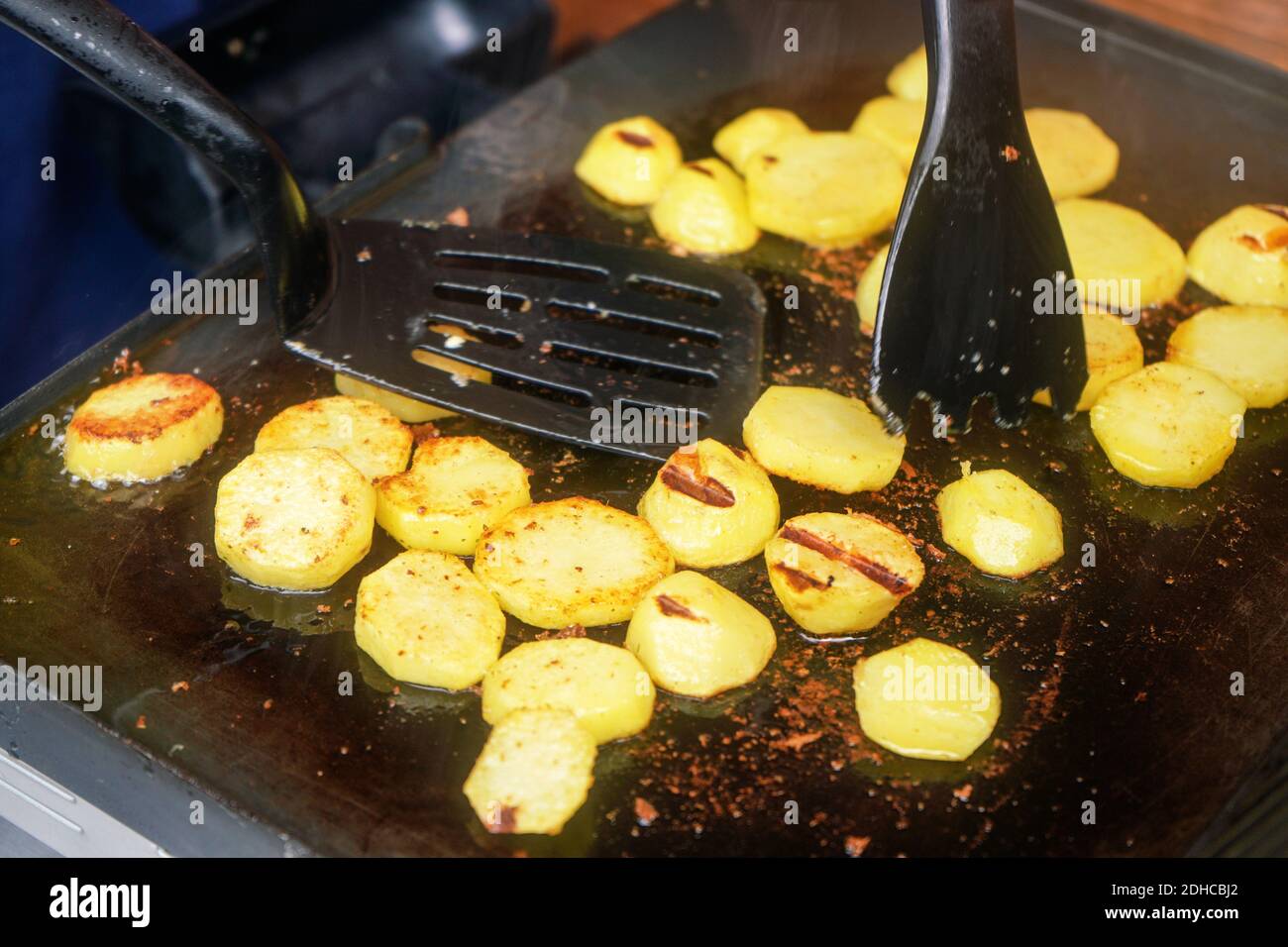 Kartoffeln in kleine Kreise geschnitten, gewürzt mit Gewürzen, gegrillt auf elektrischem Grill Stockfoto