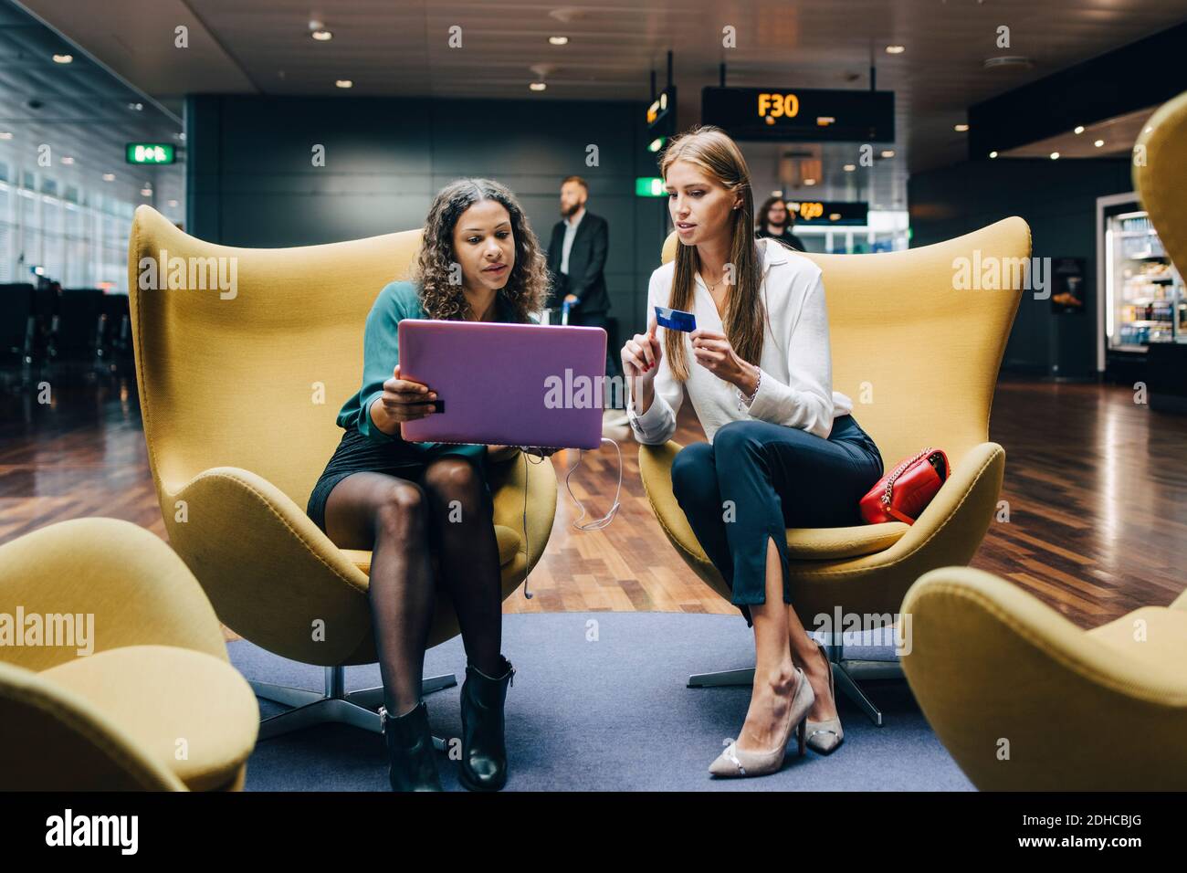 Die gesamte Länge der weiblichen multiethnischen Kollegen diskutieren über Laptop und Kreditkarte beim Sitzen in der Flughafenlobby Stockfoto