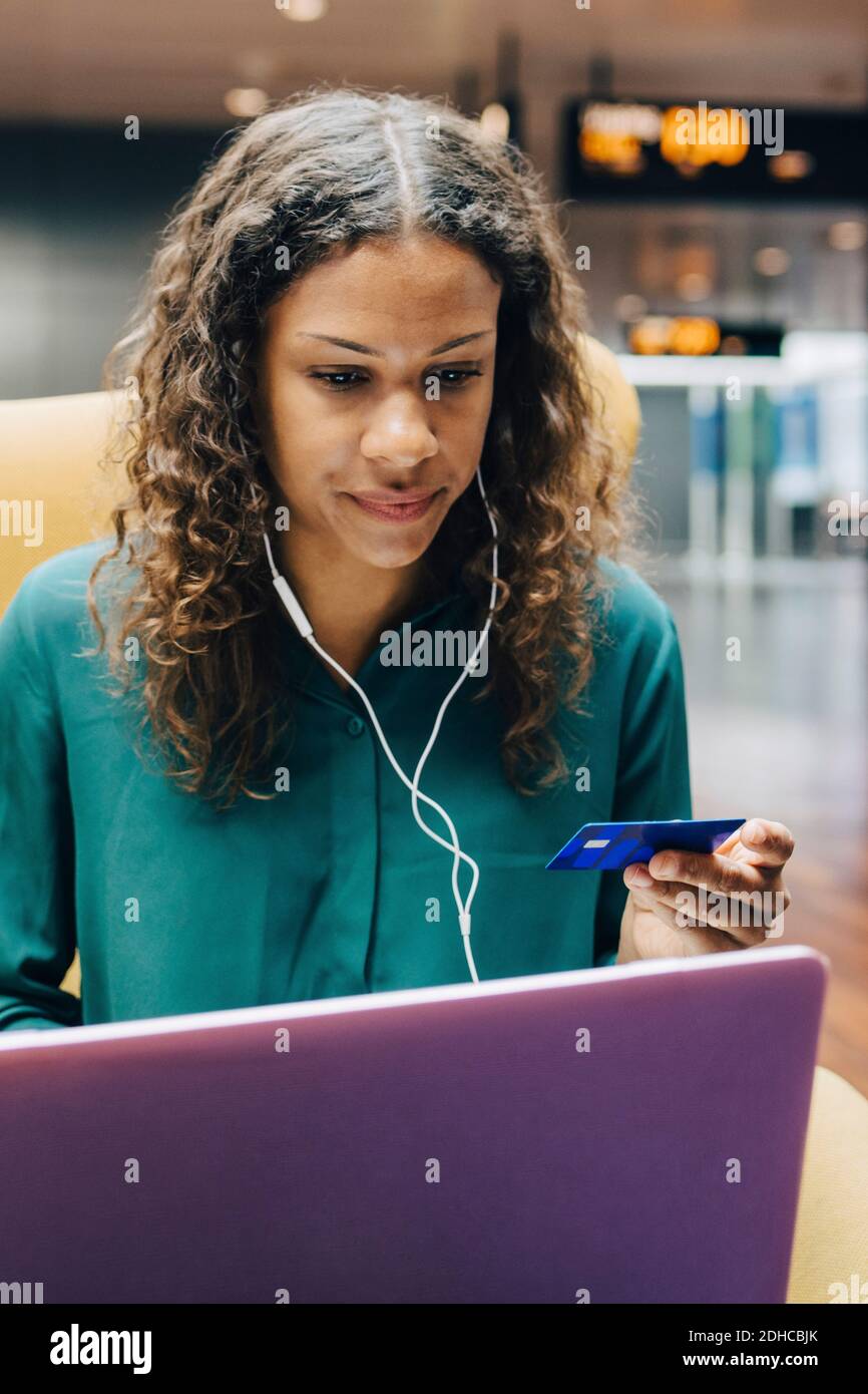 Selbstbewusste Geschäftsfrau hält Kreditkarte, während mit Laptop von Frau Kollege in der Flughafenlobby Stockfoto