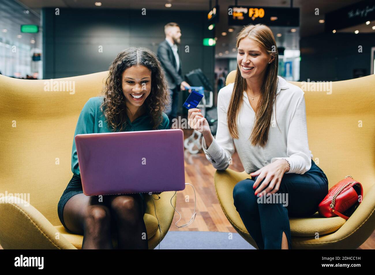 Lächelnde, multiethnische Kollegen diskutieren über Laptop und Kreditkarte Beim Sitzen in der Flughafenlobby Stockfoto