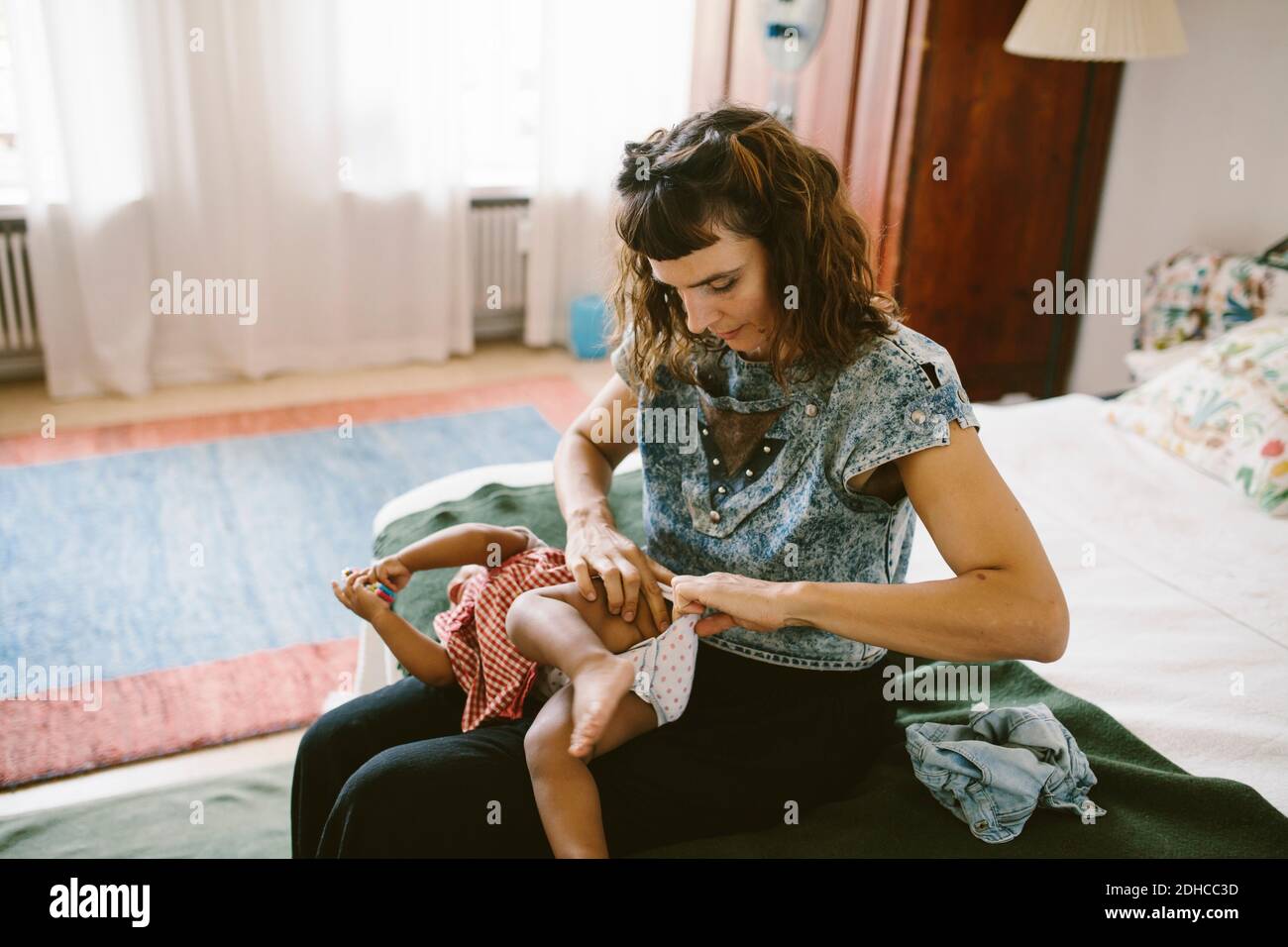 Mutter, die Windel der Tochter anpasst, während sie auf dem Bett sitzt Zu Hause Stockfoto