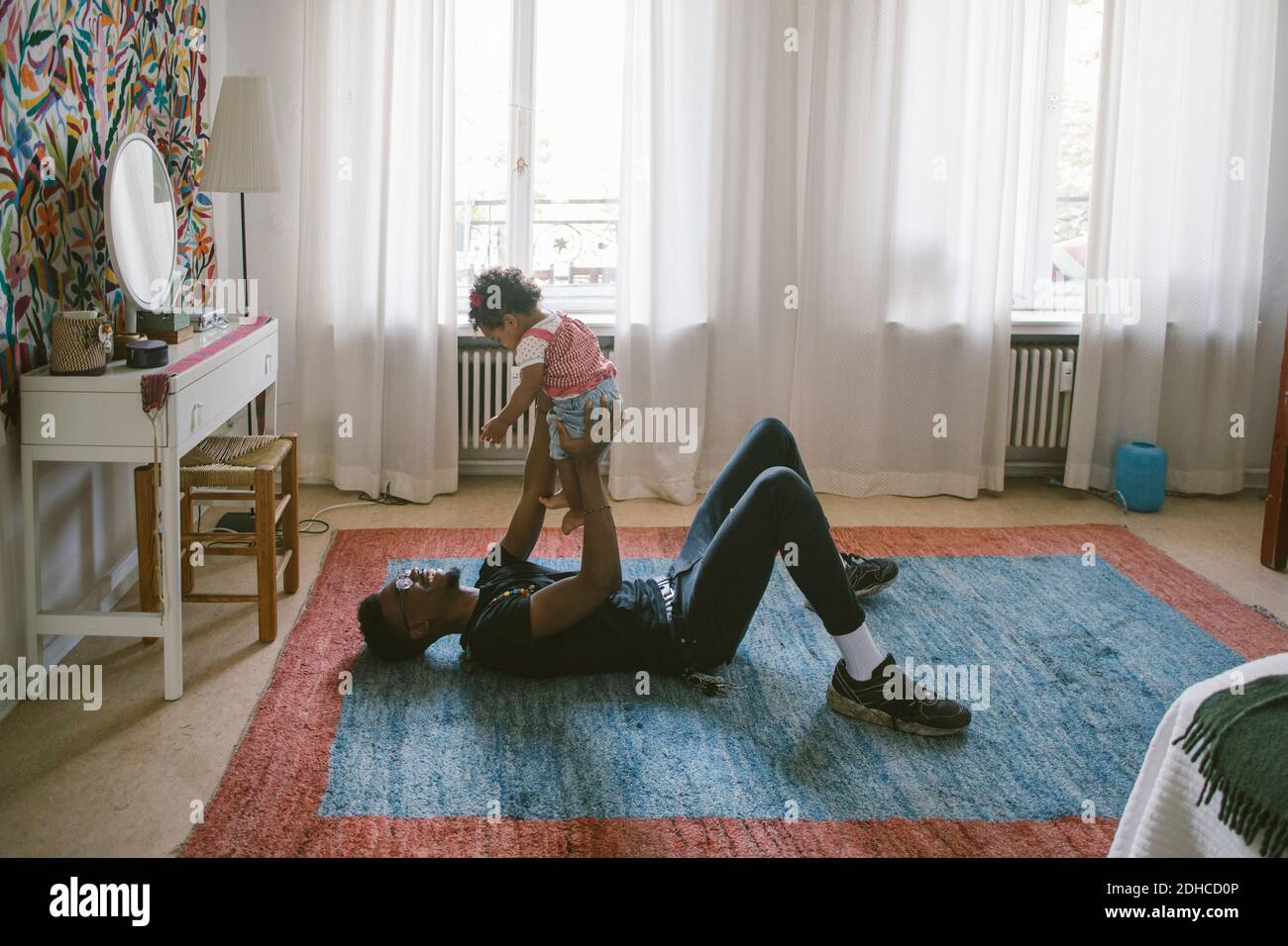 Verspielter Vater hebt Tochter, während sie auf dem Teppich zu Hause liegen Stockfoto