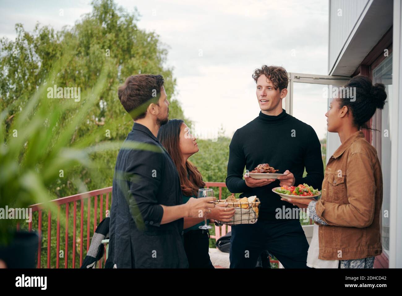 Junger Mann im Gespräch mit Freunden während der Mahlzeit während der Party Auf der Terrasse Stockfoto