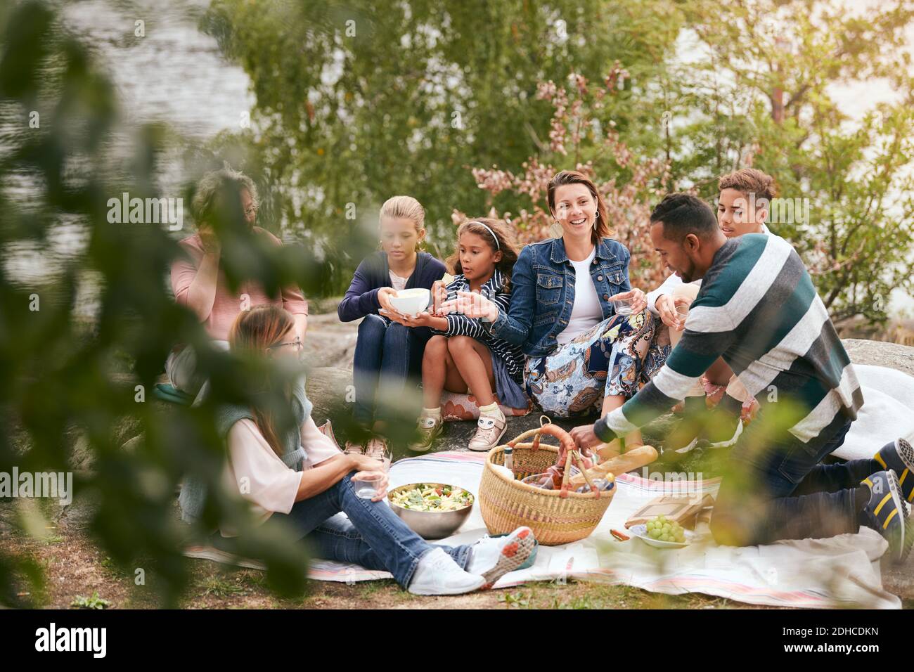 Glückliche Familie und Freunde essen am Seeufer im Park Stockfoto