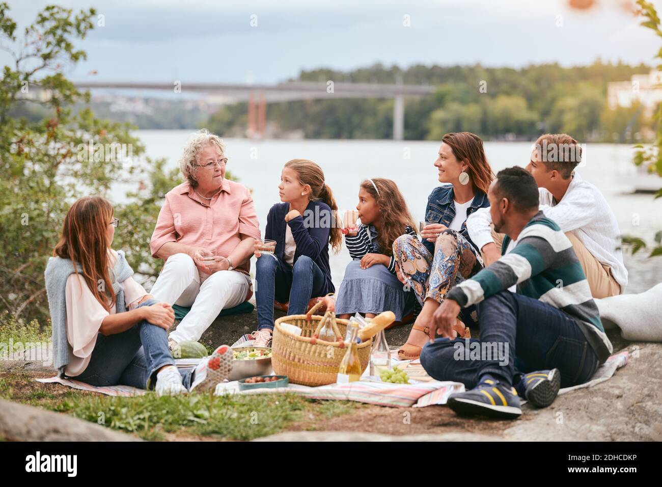 Familie und Freunde, die ältere Frau betrachten, während sie darauf sitzen Seeufer im Park Stockfoto